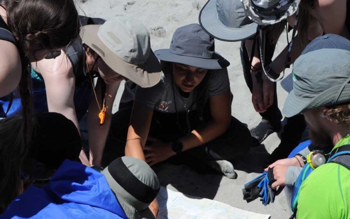 A group of people wearing sun hats and life jackets examine a map on the ground